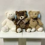 Three plush teddy bears sit side by side on a white shelf.