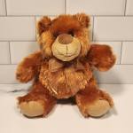 Brown plush teddy bear with a ribbon bow sitting against a tiled wall