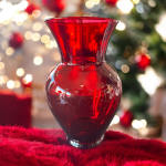 Red glass vase on a red fur surface with blurred holiday lights behind it