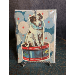Decorative card with a puppy sitting on a drum against a floral pattern