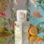 Lit white candle on a floral-patterned box with sliced lemon beside it