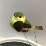 Decorative green and yellow bird figurine on thin wire legs