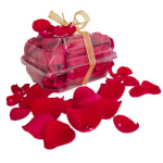 Clear gift box filled with red rose petals and tied with a gold ribbon