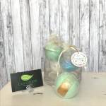 Three pastel bath bombs in clear gift packaging with a small shop card
