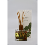Square glass reed diffuser with bay leaves and red berries in front of matching illustrated box