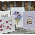 Set of four floral and birthday greeting cards displayed on a wooden surface