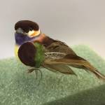 Small colorful bird figurine with brown and purple feathers on a green base