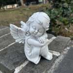 White angel figurine sitting with folded arms outdoors