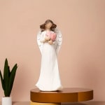 White angel figurine holding a pink heart on a pedestal