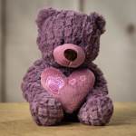 Purple teddy bear holding a pink heart