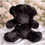 Black plush teddy bear with a ribbon bow sitting in front of blurred flowers