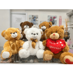 Three teddy bears with bows and a heart pillow on a shop counter