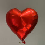 Red heart-shaped foil balloon against a plain background
