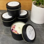 Black tins of wild peony candles, one open with dried flower petals on top