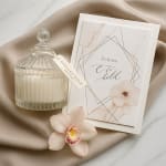Glass candle jar beside a floral wedding card with a pale orchid bloom