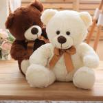 Two teddy bears with brown ribbons sit on a wooden table.