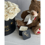 White roses in a black box beside a teddy bear and candle