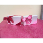 Two white gift boxes with red and pink ribbon bows on a pink surface