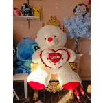 Large teddy bear holding a heart pillow beside a vase of blue flowers