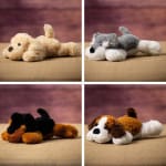Four small plush dog toys in different colors on a fabric surface.