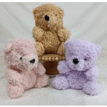Three fluffy teddy bears in pink, tan, and lavender sit on a small wooden stand.