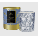 A scented candle in a patterned gold-and-blue box beside a faceted glass candle jar