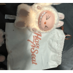 Plush lamb toy lying on a white bag with pink text