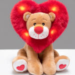Plush teddy bear holding a red heart-shaped pillow with lights
