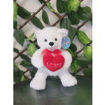 White teddy bear holding a red heart with a leafy backdrop