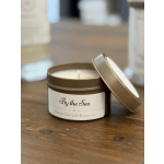 Brown tin candle labeled "By the Sea" on a wooden table