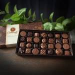 Open box of assorted milk and dark chocolates on a wooden surface with leafy accents