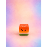 Small orange cube-shaped candle with a face design on a pastel background