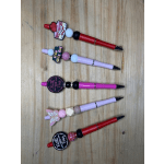 Five decorated pens with beads and charms arranged on a wooden surface.