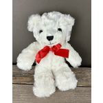 White plush teddy bear with a red bow sitting on a wooden surface
