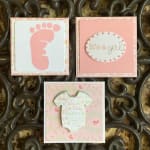 Three pink baby shower cards with a footprint, "It's a girl," and a onesie.