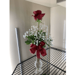 Single red rose in a clear glass vase with white baby's breath and a red ribbon