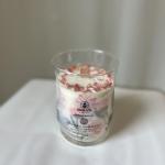 A clear glass candle jar with white wax and pink petals