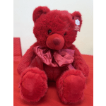 Red teddy bear with a satin bow sitting on a red surface