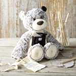 Plush teddy bear holding a small gift box beside a glass jar with sticks
