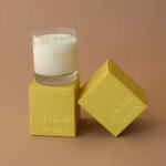 White candle in a glass tumbler on yellow boxes