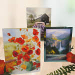 Three floral greeting cards with poppy and landscape designs on a table.