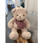 A plush teddy bear with a red gingham bow sits on a wooden bench.