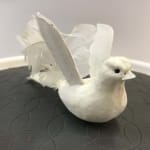 White decorative bird figurine with raised wings on a dark textured surface
