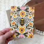 Floral greeting card with a bee illustration held in a hand