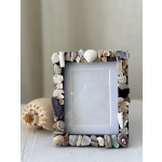 Shell-covered photo frame on a table with a seashell ornament behind it