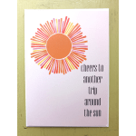 Greeting card with stylized orange sunburst and text 'cheers to another trip around the sun'