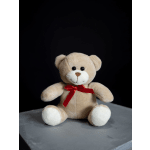 Beige teddy bear with a red ribbon sitting on a gray surface