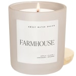 Lit beige candle in a glass jar labeled Farmhouse