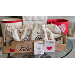 Gift bags in a cardboard tray with heart-themed cards and mugs behind them.