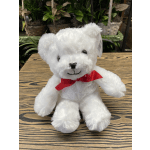 White teddy bear with a red ribbon sitting on a wooden surface